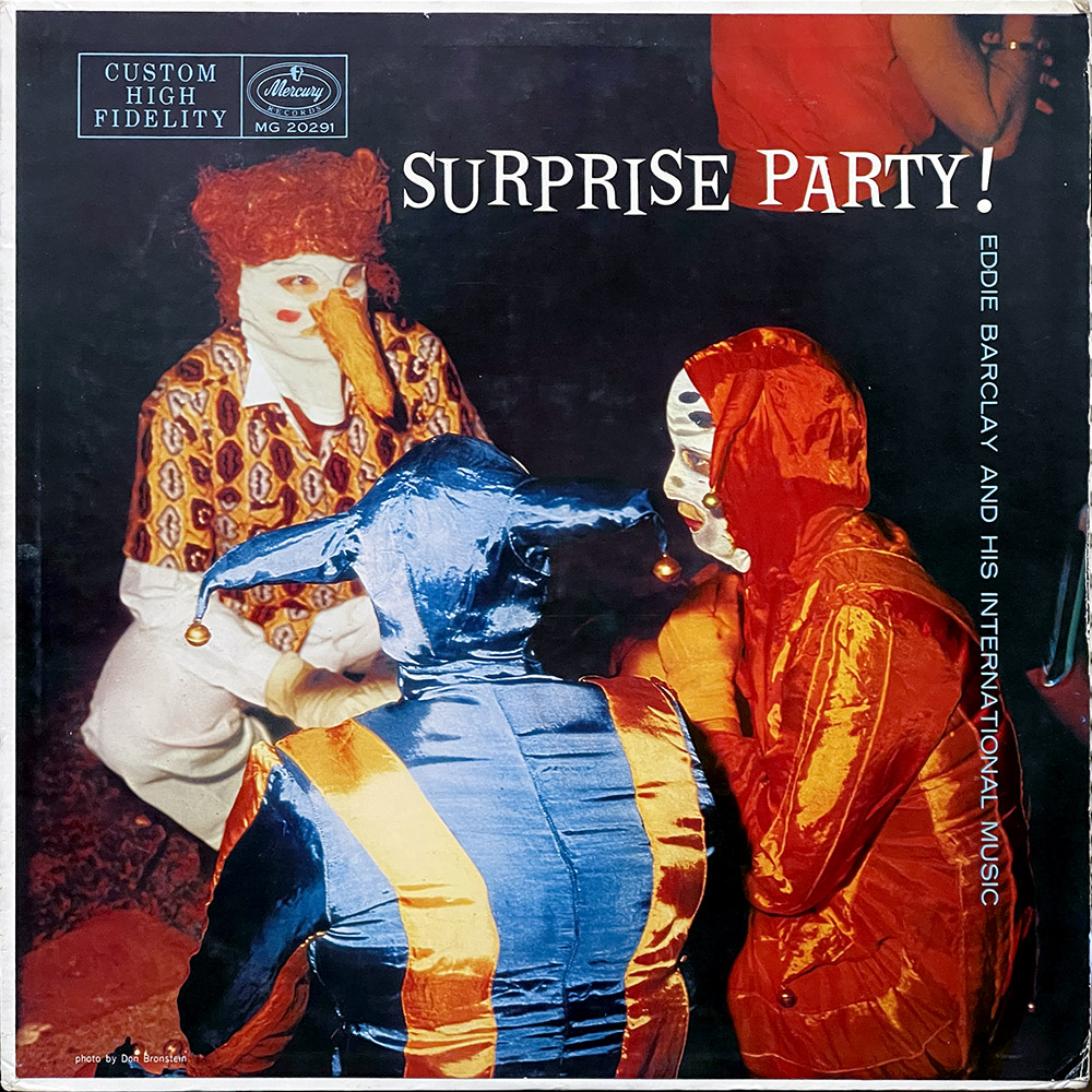 The album cover for "Surprise Party!" by Eddie Barclay and His International Music features a photograph of people in colorful, elaborate costumes. One person is wearing a blue and gold jester outfit, while another is dressed in a red and gold costume with a mask that has a long, pointed nose. A third person, partially visible, is wearing a red wig and a patterned shirt. The background appears to be dimly lit, creating a mysterious and festive atmosphere. The album title is written in bold white letters at the top right, and the artist's name is displayed vertically on the right side. The Mercury Records logo and the text "Custom High Fidelity" are located in the top left corner.