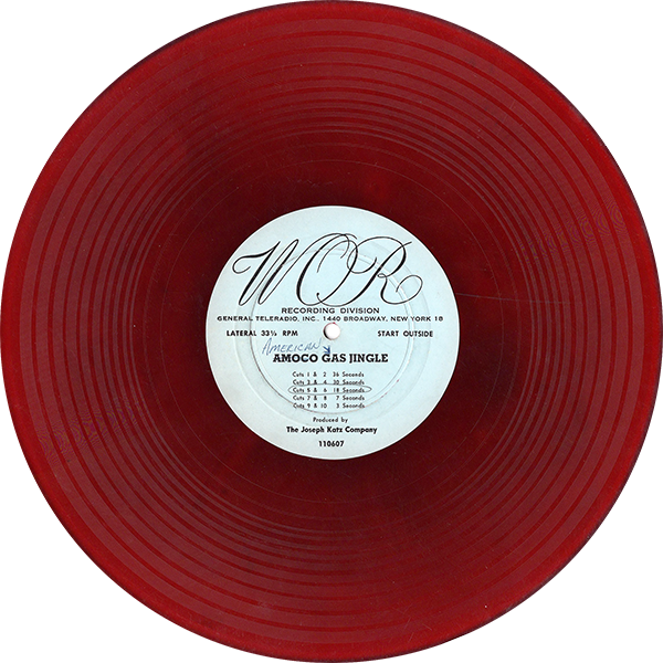 The image shows a red vinyl record with a white center label. The label reads "WOR Recording Division, General Teleradio, Inc., 1440 Broadway, New York 18" at the top, with the text "Amoco Gas Jingle" written below. The label also lists several cues with their corresponding durations in seconds (e.g., "Cues 1 & 2: 60 Seconds"). At the bottom, the label notes that the record was "Produced by The Joseph Katz Company" with the number "118067" displayed at the very bottom. The vinyl has a translucent red color, and the label suggests that this record was likely used for broadcasting a jingle.