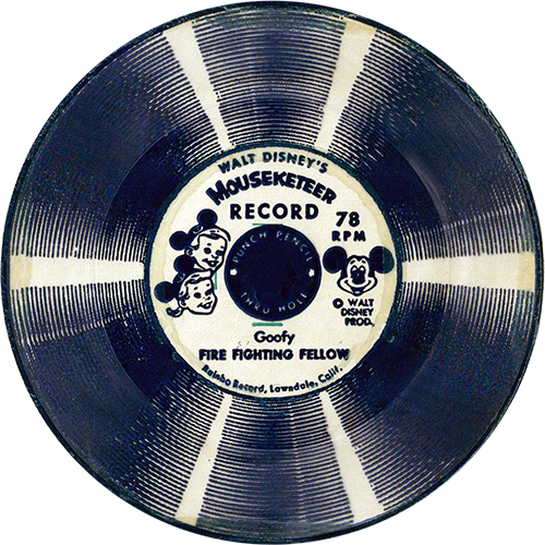 The image is of a vintage Walt Disney’s Mouseketeer Record, specifically a 78 RPM flexi-disc. The label in the center features drawings of a boy and a girl wearing Mickey Mouse ear hats, representing Mouseketeers. The text on the label reads “Walt Disney’s Mouseketeer Record” and includes a picture of Mickey Mouse. The title of the record is "Fire Fighting Fellow." The record itself has a circular design with alternating light and dark bands, creating a striped appearance. The label mentions "Punch Pencil Thru Holes" and indicates that it was produced by "Rainbo Records, Lawndale, Calif." The record is intended to be punched through the center for use, likely in a children's phonograph or similar device.