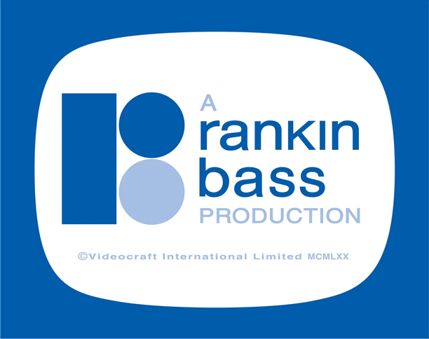 The image shows the logo for "A Rankin/Bass Production," a well-known animation company. The logo features a stylized design with two blue shapes on the left side: a rectangle and a circle stacked vertically. To the right of these shapes, the text reads "A rankin/bass PRODUCTION" in a modern sans-serif font, with "rankin" and "bass" in bold and the word "PRODUCTION" underneath in smaller, lighter text. The background is a blue rectangle shaped like an old-fashioned television screen. Below the main text, the copyright notice reads "© Videocraft International Limited MCMLXX," indicating the logo is from 1970. Rankin/Bass is famous for its stop-motion holiday specials, such as "Rudolph the Red-Nosed Reindeer."